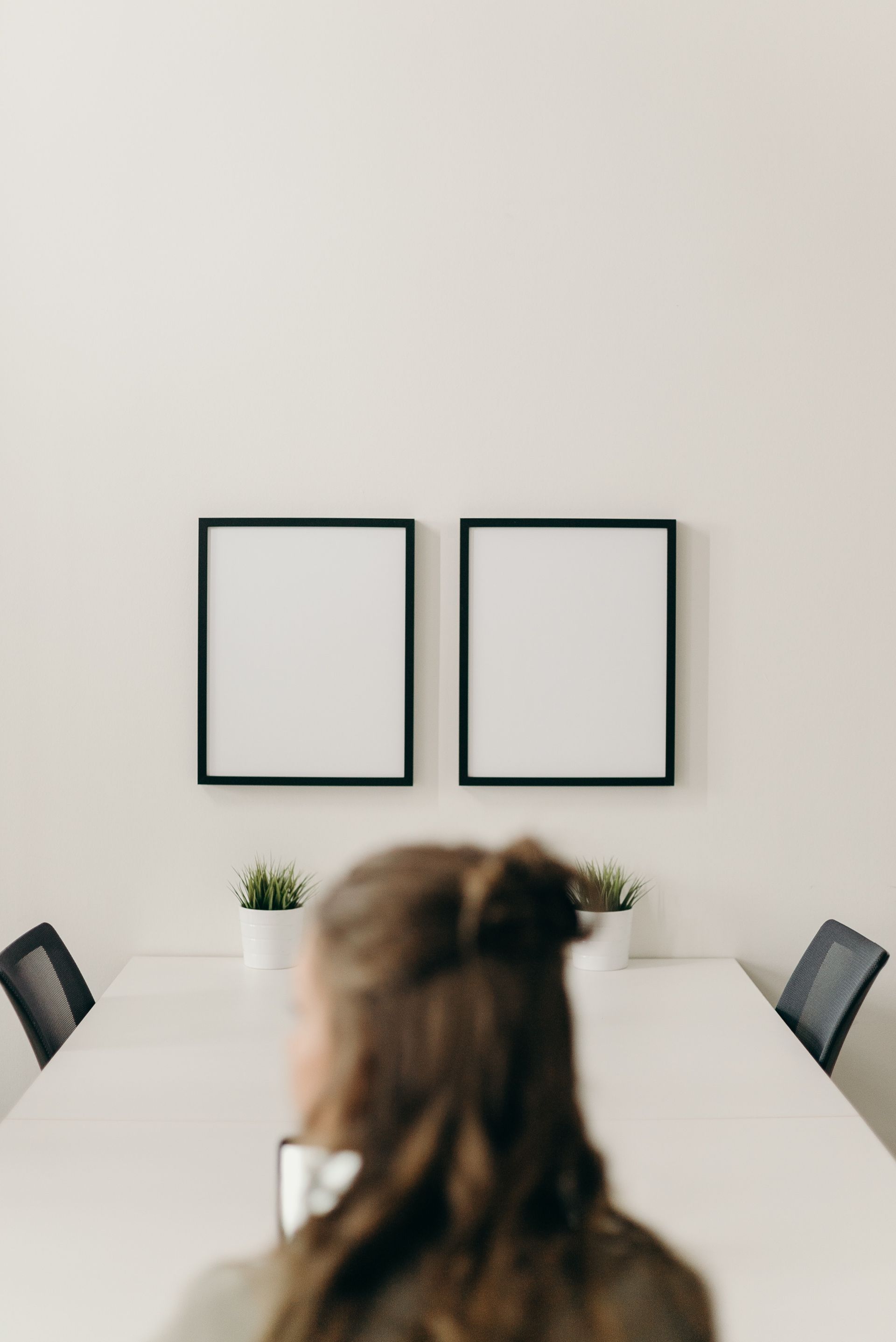A woman looking to the side with two empty frames hung on the wall