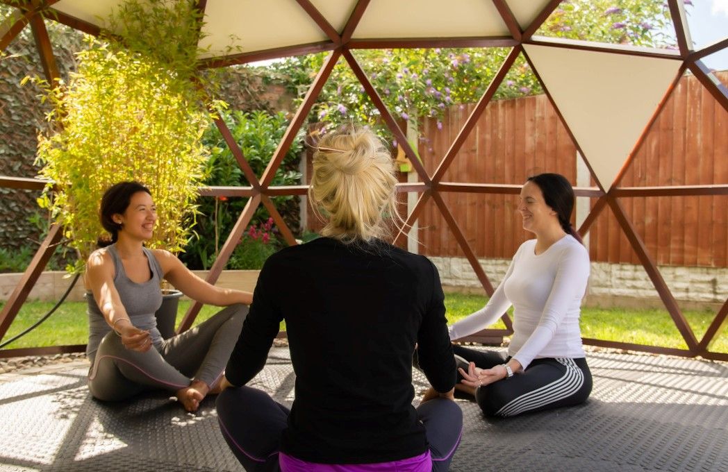 3 women doing yoga under dome in garden