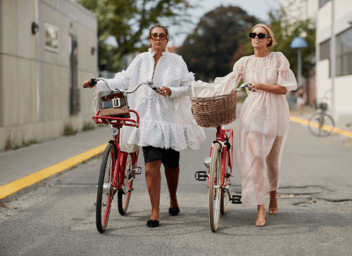 Two women wearing white dresses pushing bicycles