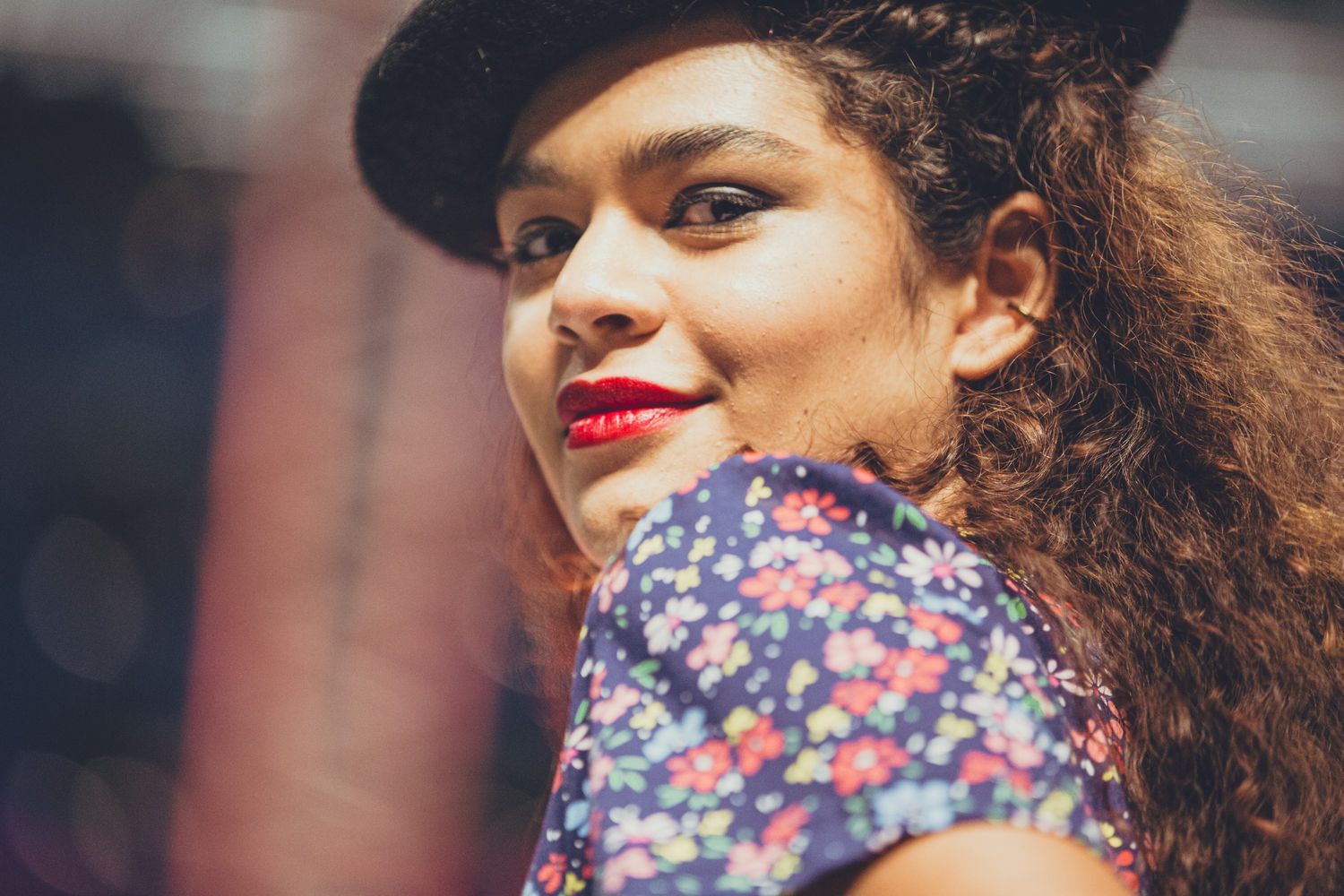Close up of a female model wearing red lipstick and looking over her shoulder at the camera with a small smile
