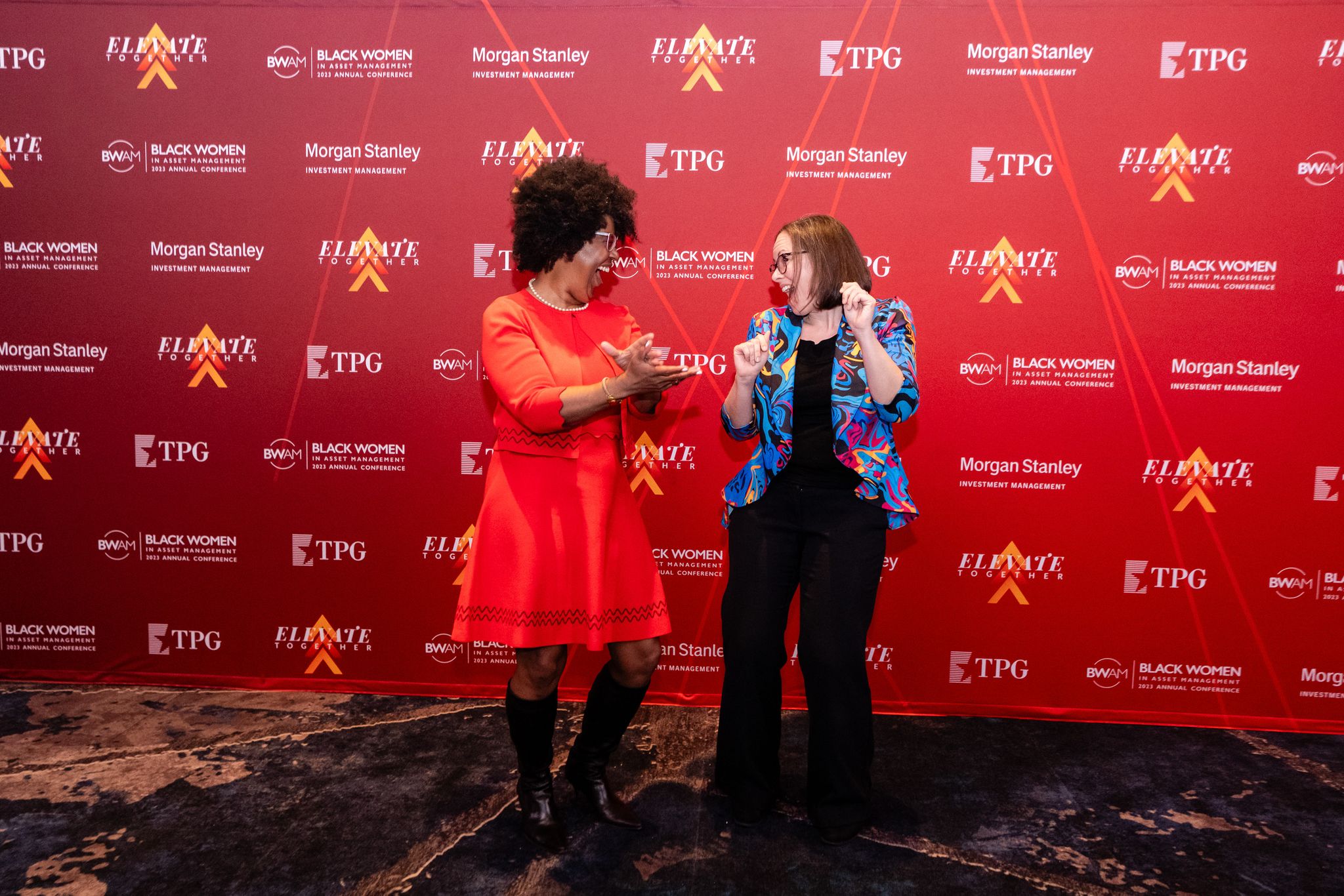 Two women dancing in front of the Elevate Together Conference backdrop
