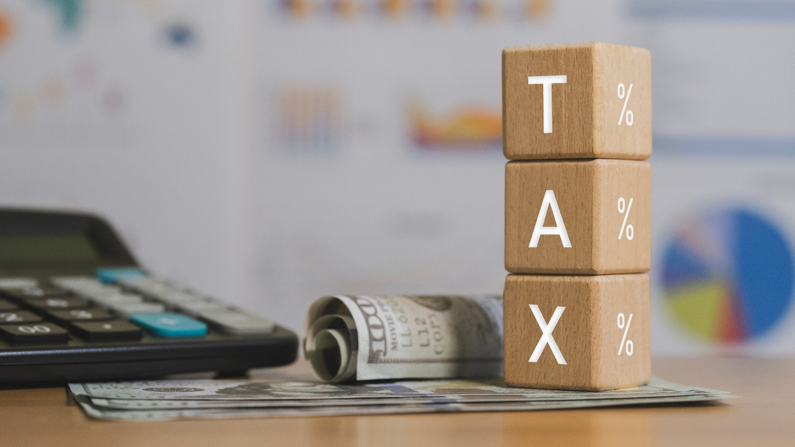 Wooden blocks spelling “TAX” stacked beside cash and calculator, representing income deductions and 2026 federal tax changes.