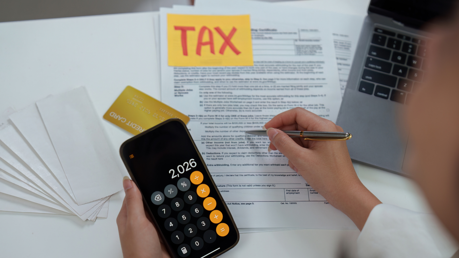 Person calculating taxes on smartphone with IRS forms and credit card, representing 2026 tax filing and reporting requirements.