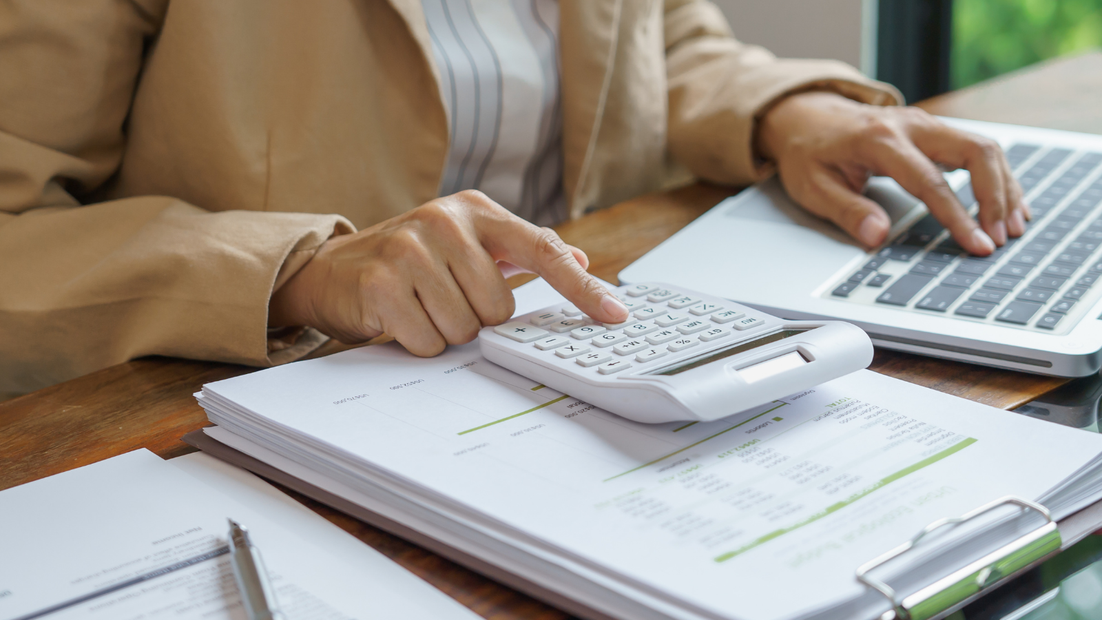 Business owner using calculator and laptop to review expenses, illustrating Section 179 deduction updates for 2026.