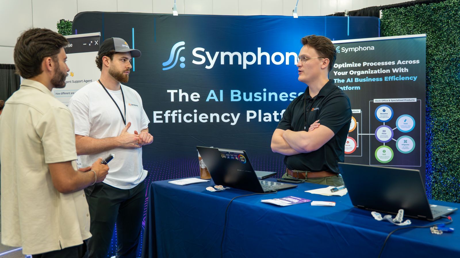 A member of staff for Symphona discussing their product with two trade show attendees