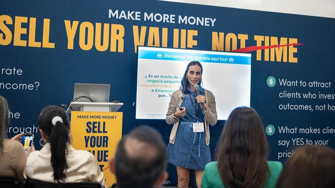 A woman giving a masterclass at The Business Show Miami. He is wearing jeans, a t shirt and a cap, holding a microphone. Behind him is a wall covered in purple branding for his company CREATIVO