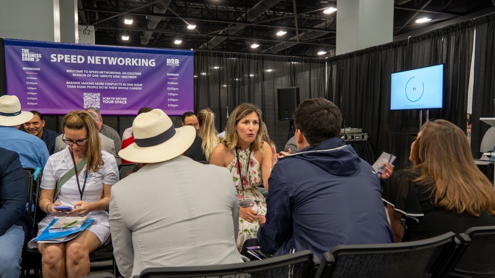 An image of multiple people sat down talking facing each other. A sign in the background says 'Speed Networking'