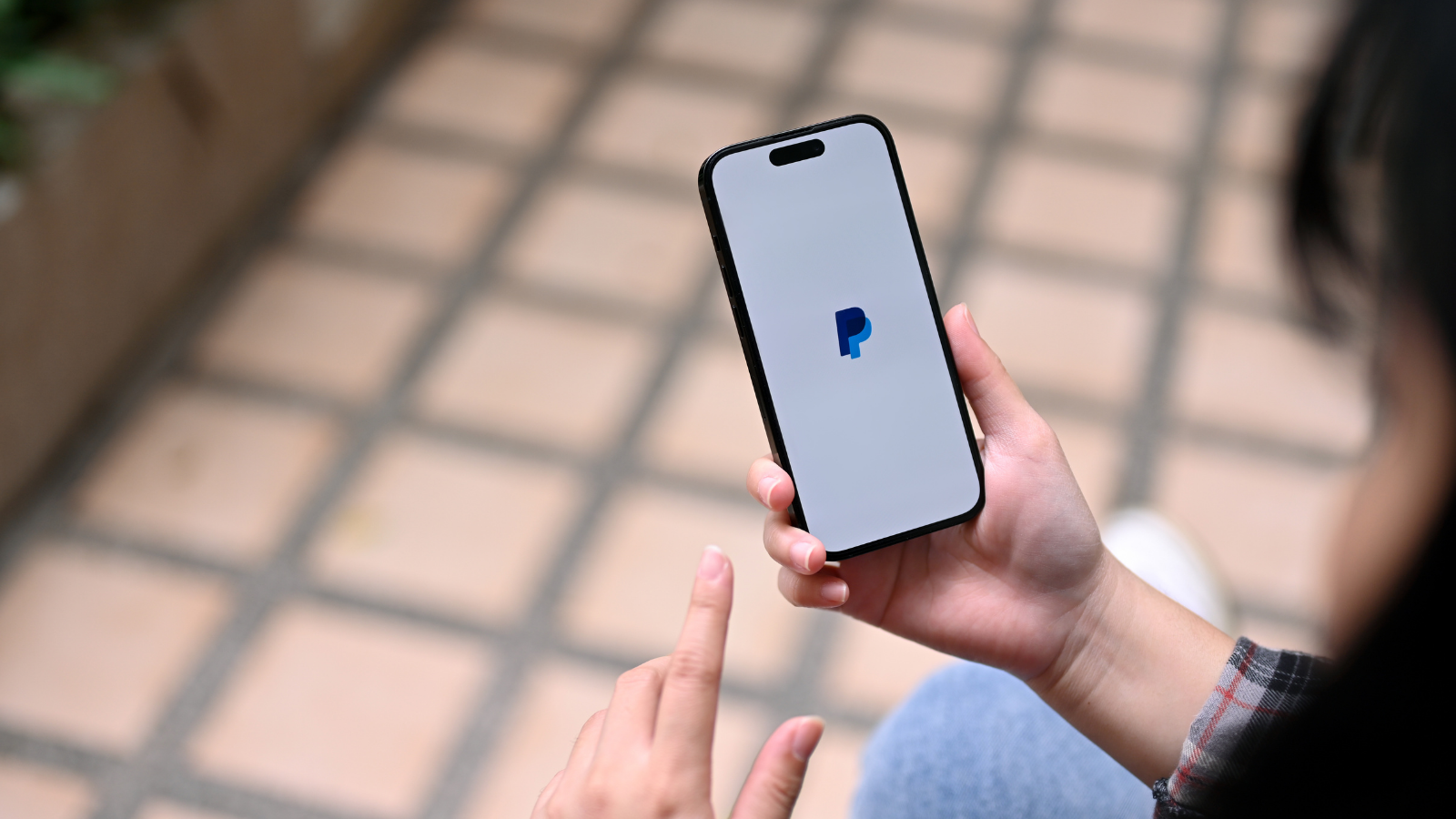 A person holding a phone with the PayPal logo on the screen