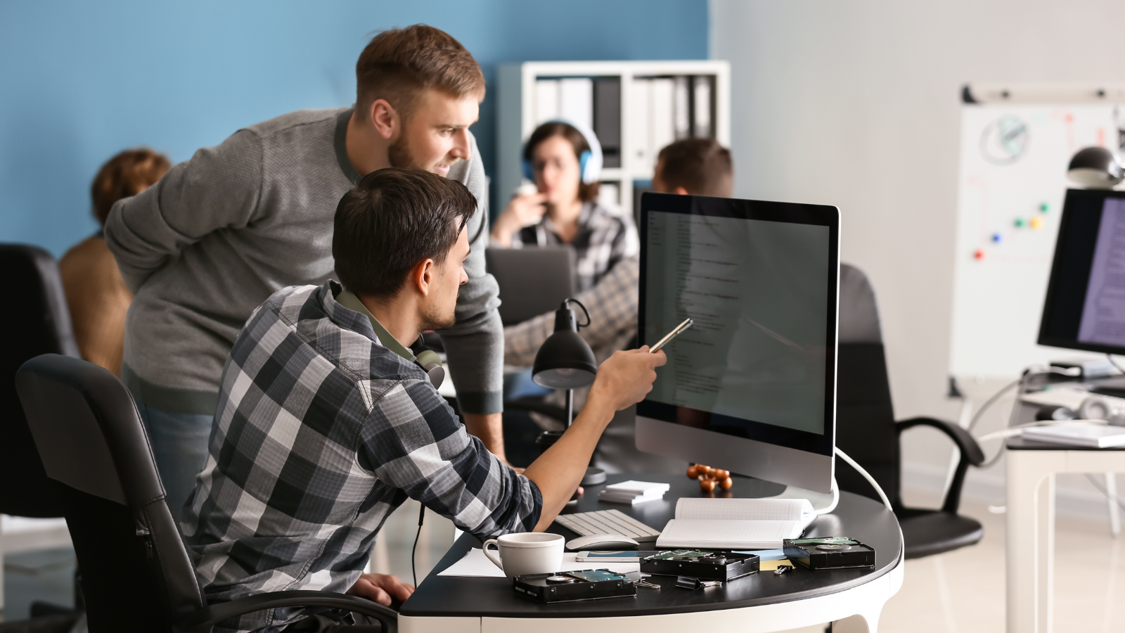 A man looking over another man's shoulder, helping him with his computer