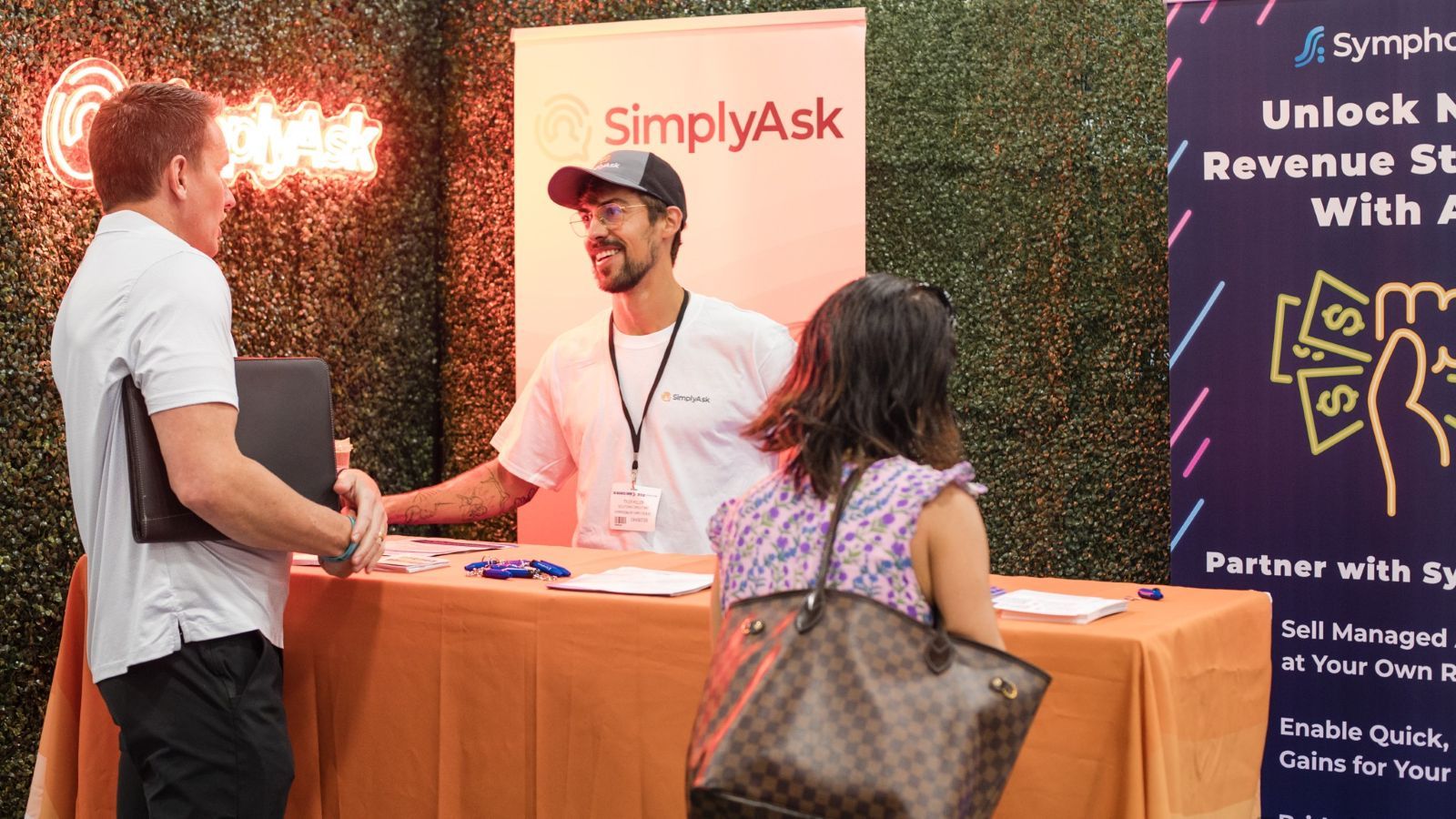 A picture of two men talking, one is behind a table, exhibiting with SimplyAsk