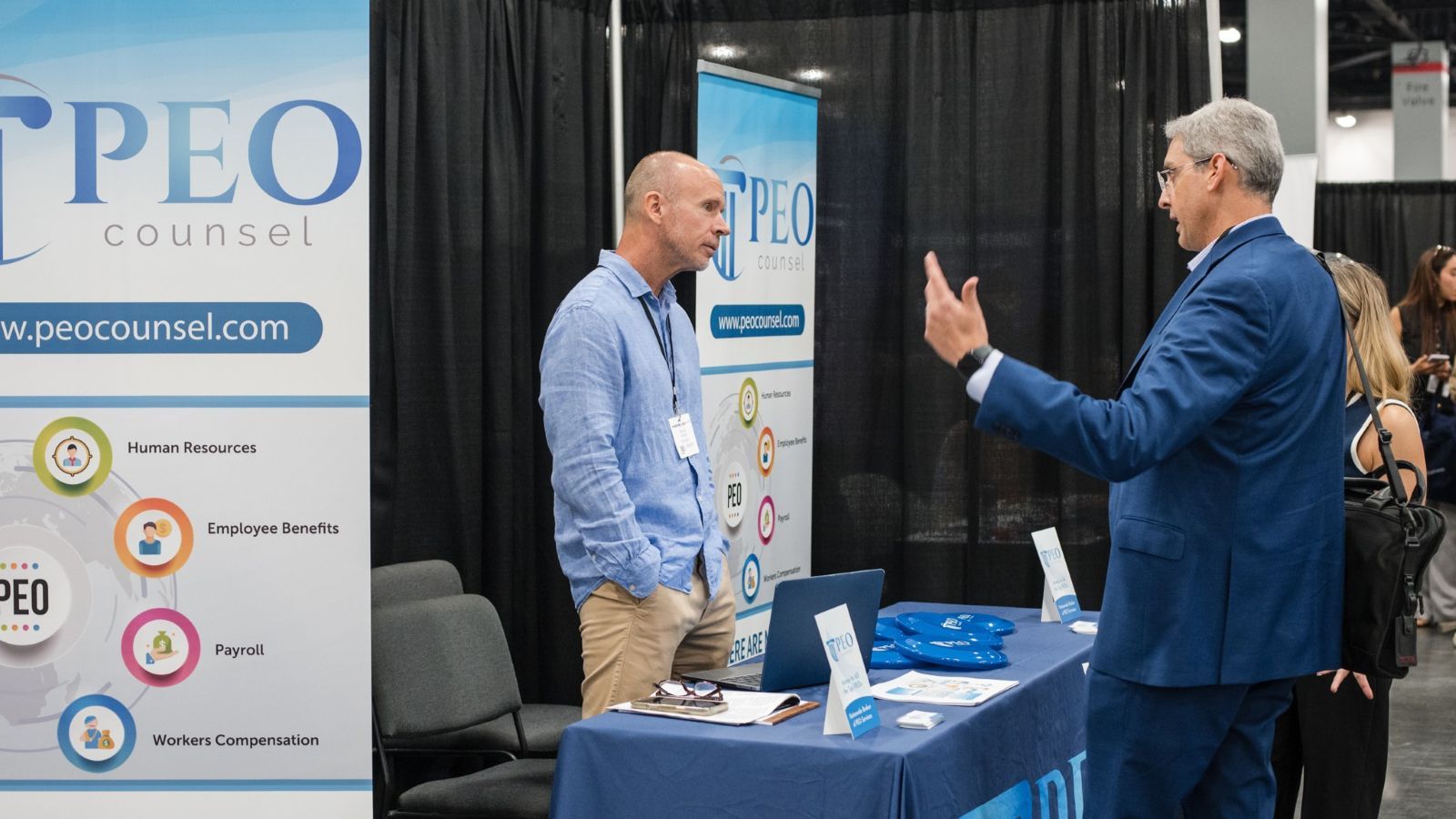 A picture of two men talking, one is behind a table, exhibiting with SimplyAsk