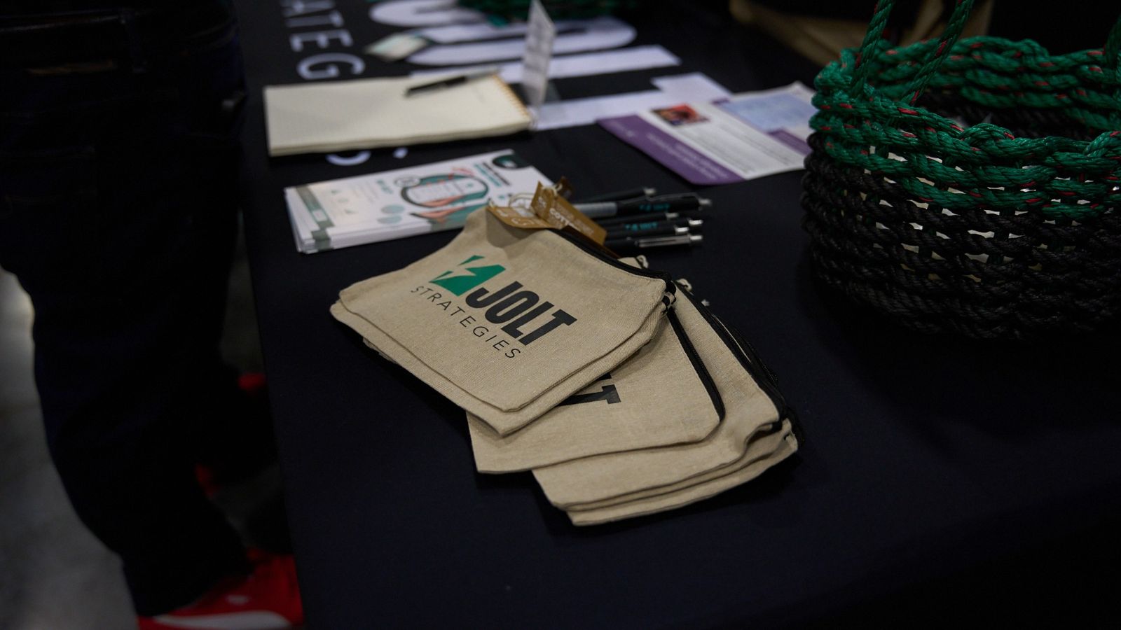 A table at a trade show full of merchandise for Jolt Strategies, the foreground contains tote bags