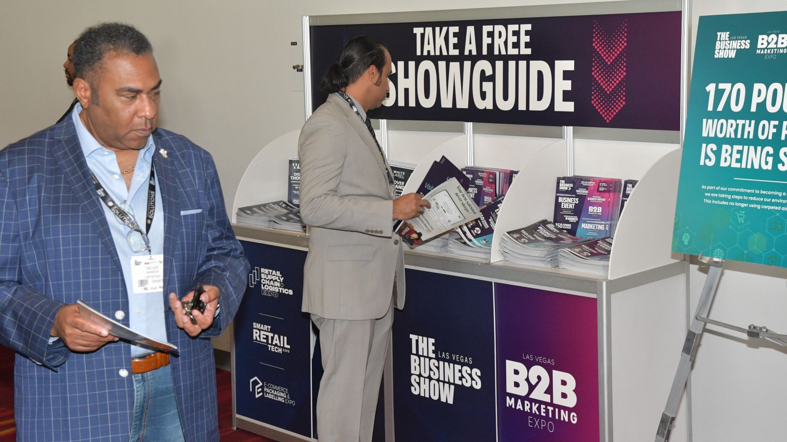 A picture of the place that you can pick up free showguides from at The Business Show, there is a man beside it reading one of the guides