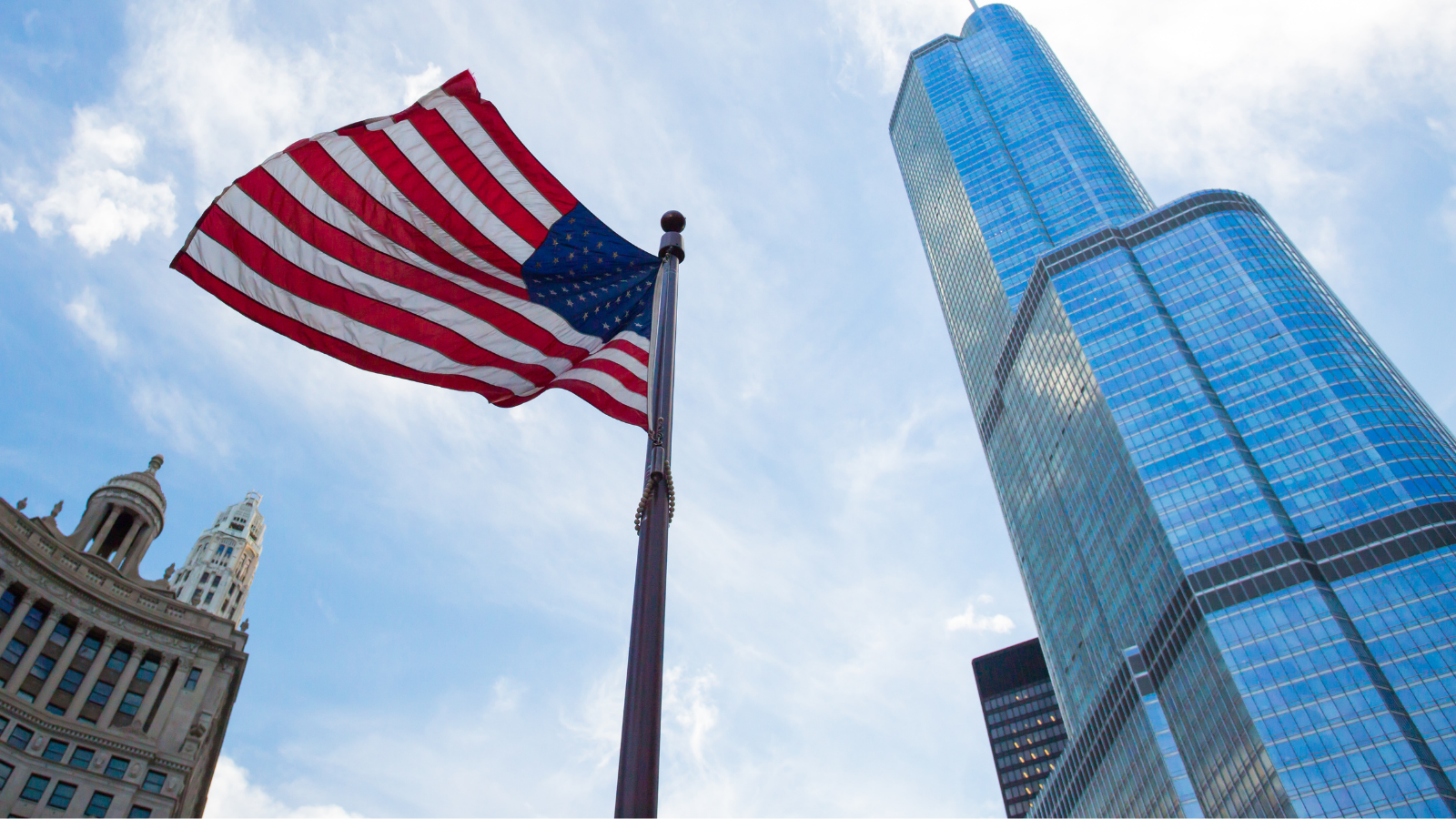 American flag waving in front of a modern US skyscraper, representing the US economy, business growth, and financial stability
