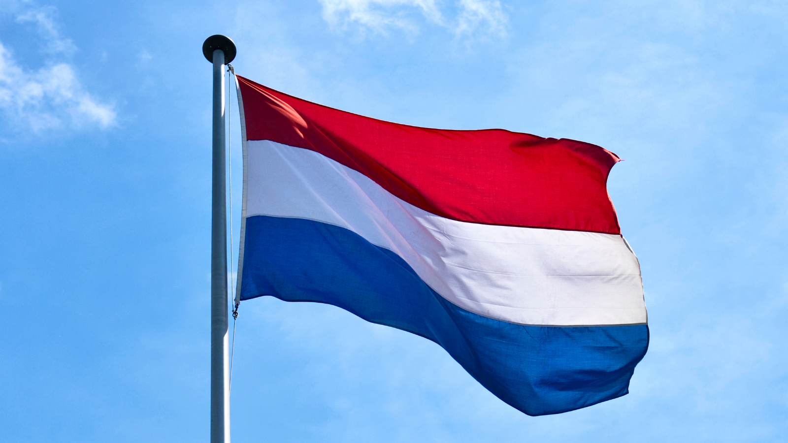 The flag of the Netherlands flying across a blue sky