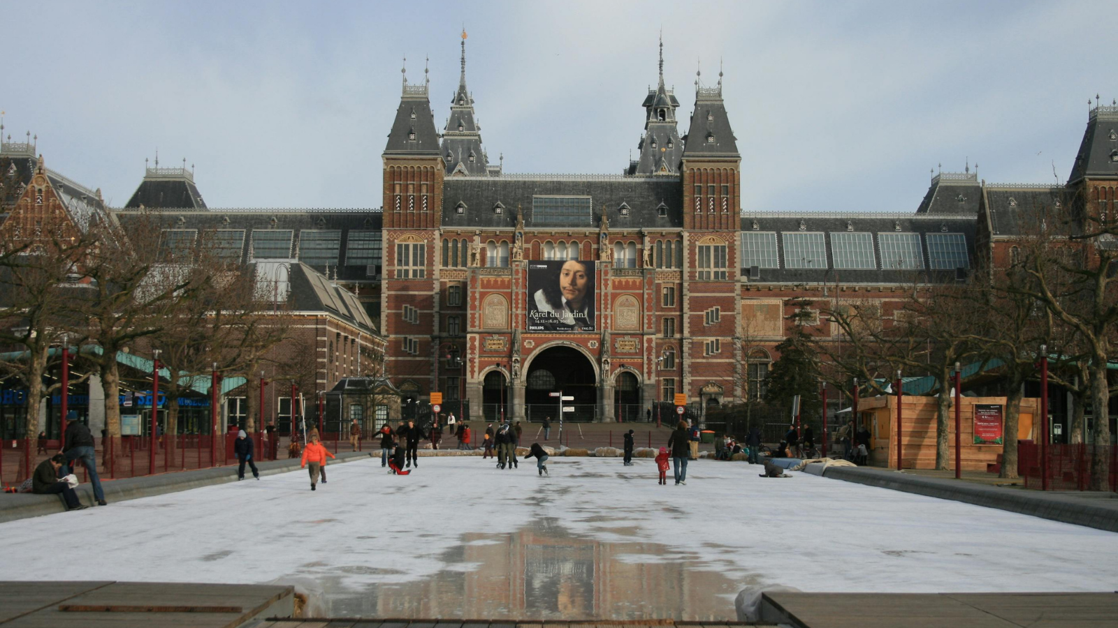 Rijksmuseum in Amsterdam with people ice skating on the frozen reflecting pool in front.