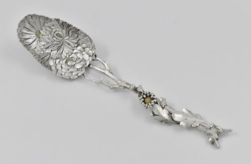 A Japanese silver Meiji period (1868 -1912) serving spoon decorated with chrysanthemums inlaid with gold, having an asymmetrical twig handle adorned with foliage and buds, by Sadajiro (of) Musashiya.