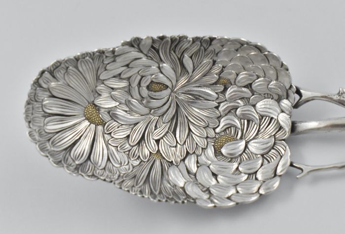 A Japanese silver Meiji period (1868 -1912) serving spoon decorated with chrysanthemums inlaid with gold, having an asymmetrical twig handle adorned with foliage and buds, by Sadajiro (of) Musashiya.