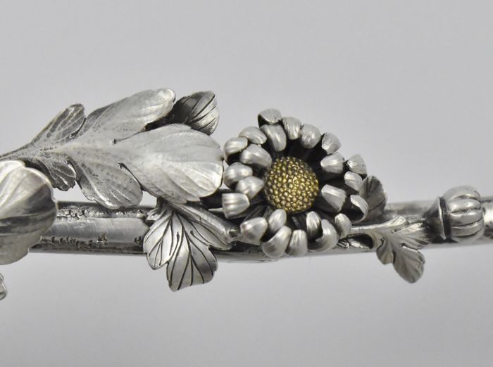 A Japanese silver Meiji period (1868 -1912) serving spoon decorated with chrysanthemums inlaid with gold, having an asymmetrical twig handle adorned with foliage and buds, by Sadajiro (of) Musashiya.