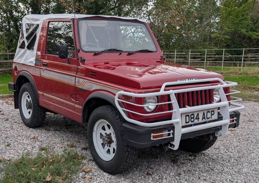 Red Suzuki SJ410 soft-top 4x4 with a white bull bar parked on gravel, featured on Tasty Classics
