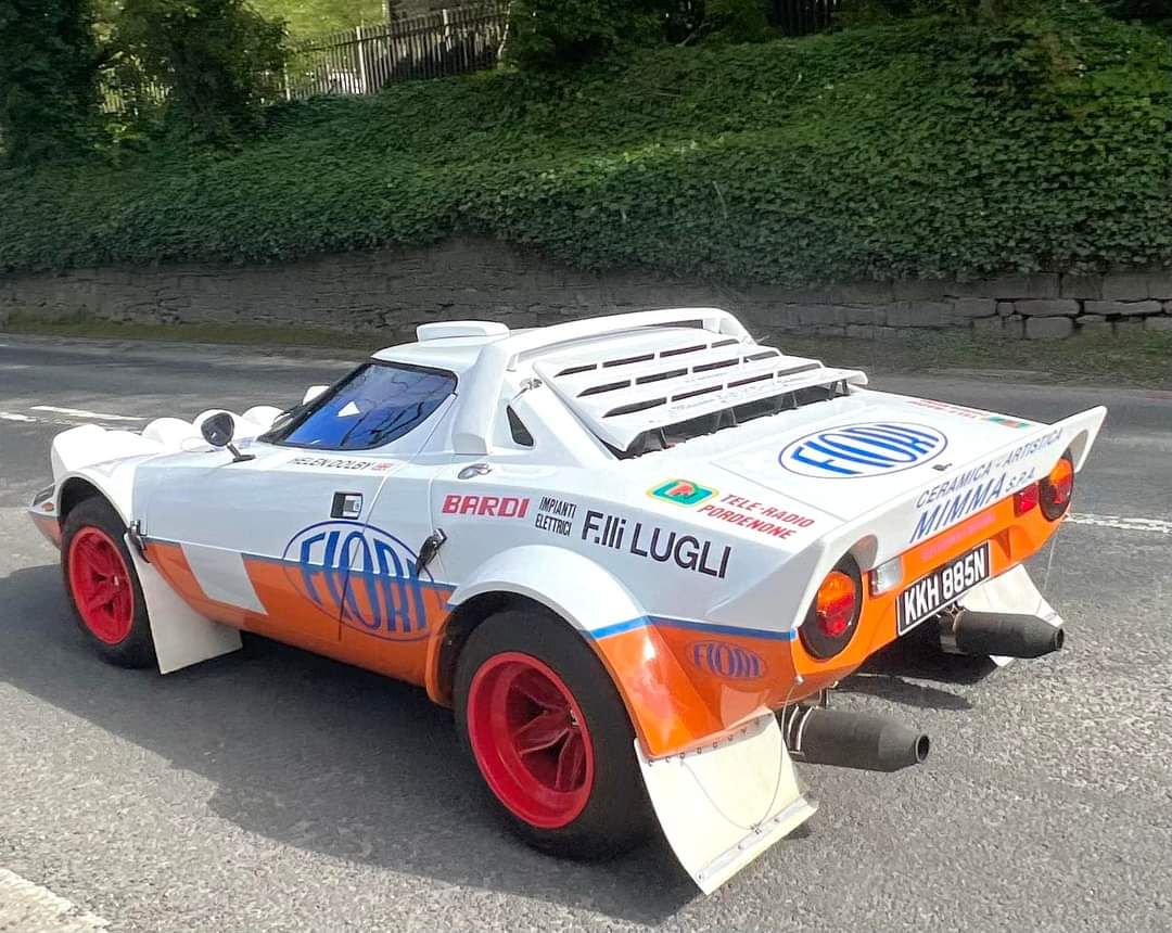 A vintage Lancia Stratos rally car in white and orange Fiorio livery with red wheels.