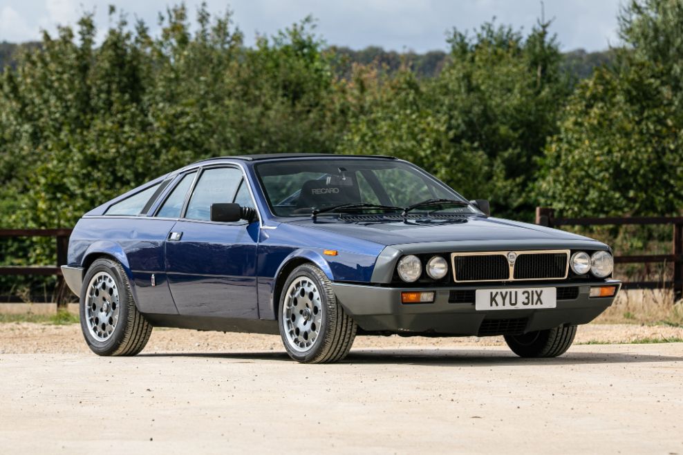 Front-three-quarter view of a dark blue 1982 Lancia Montecarlo Spider classic sports car parked on a paved ground from Grand Tour Series. 
