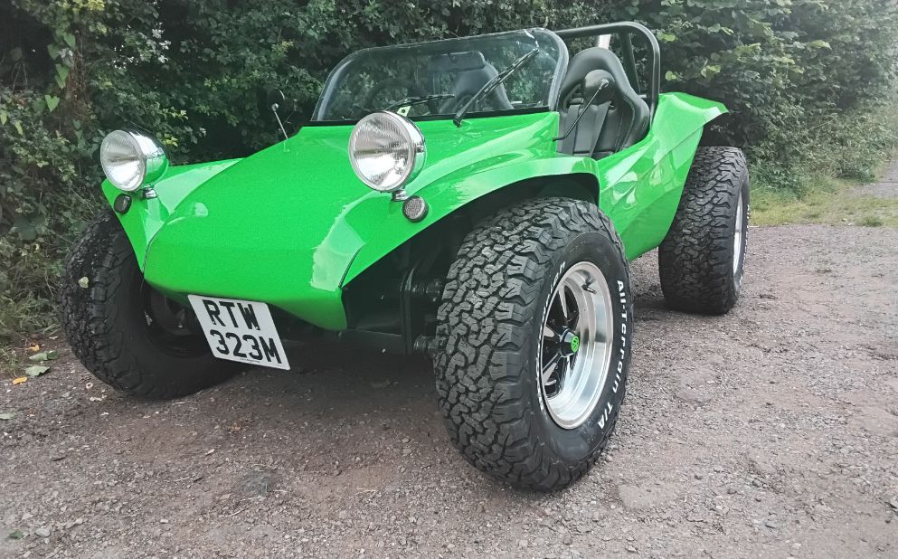 Vibrant green Volkswagen-based beach buggy with large off-road tires and a roll bar, parked on a gravel path.