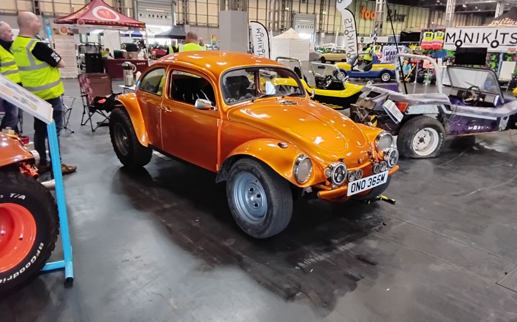 Custom orange Volkswagen Beetle Baja Bug with wide fenders and off-road tires, on display at a motor show.