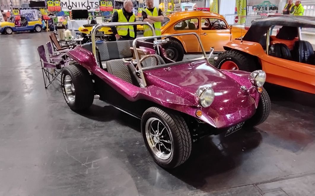 Sparkling purple Volkswagen-based custom beach buggy with roll bar and polished wheels on display at a motor show.
