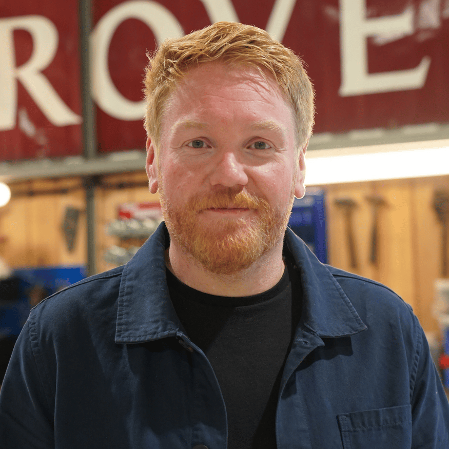 YouTuber from Tasty Classics wearing a blue jacket standing in front of a Rover workshop sign