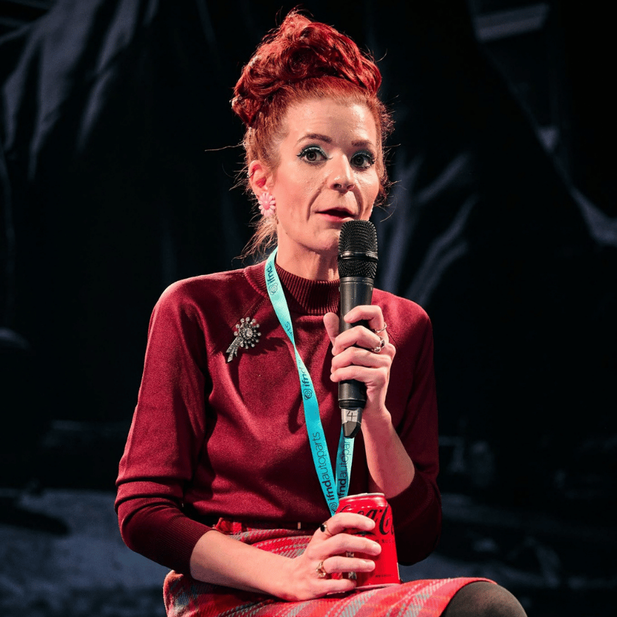 YouTuber idriveaclassic with distinctive red hair speaking into a microphone, wearing a burgundy top and holding a Coca-Cola can