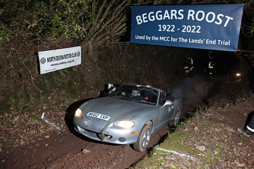 Silver Mazda MX-5 rally car tackling the muddy 'Beggars Roost' section of the Land's End Trial, a historic classic trial event by the MCC.