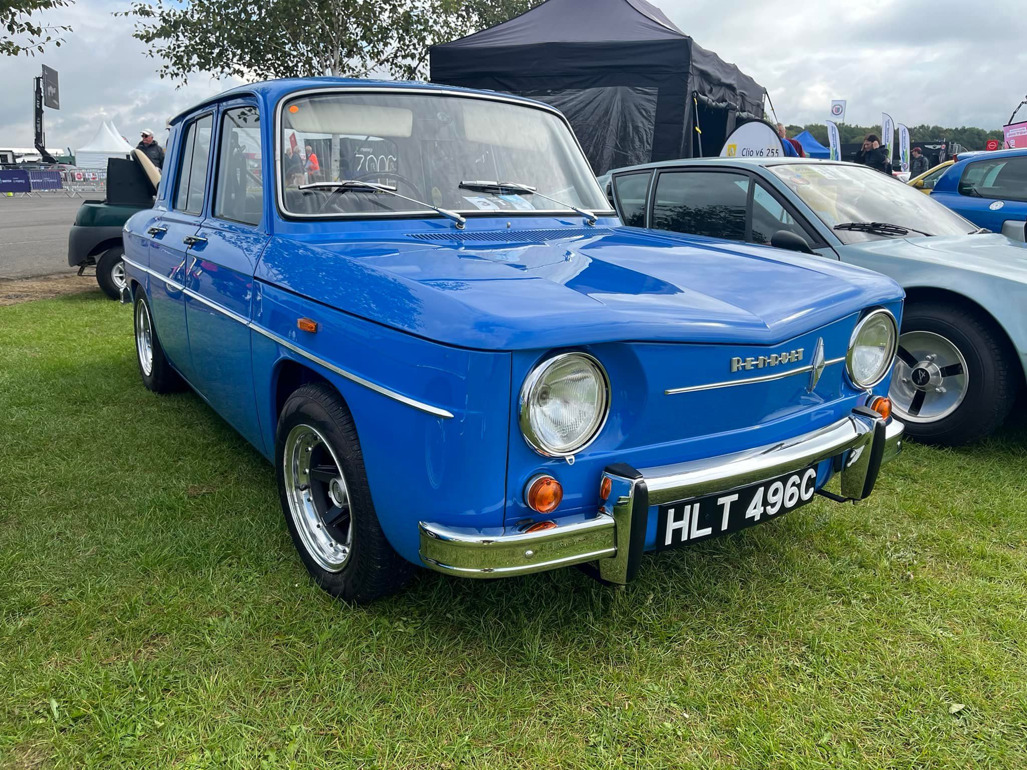 A beautifully restored bright blue classic Renault 8 or 10 sedan with chrome accents and aftermarket wheels, parked on the grass at an outdoor car show.