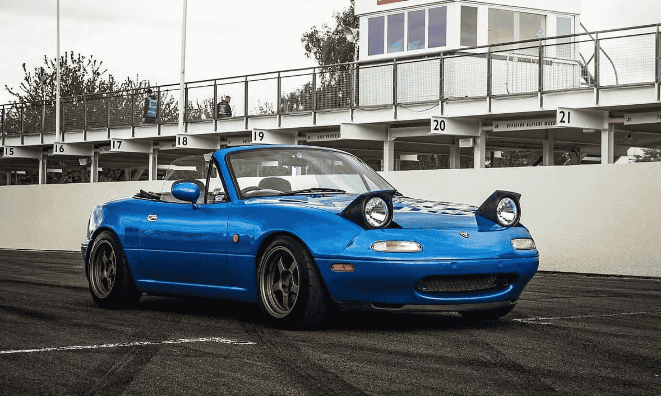 Blue Mazda MX-5 NA sports car with pop-up headlights on a racetrack, featured on Garage of Luke