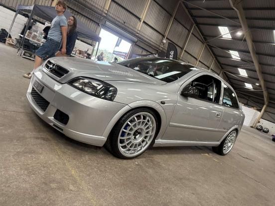 A silver lowered Vauxhall Astra H hatchback, owned by David Wootton, with multi-spoke motorsport-style wheels, displayed indoors at an event.