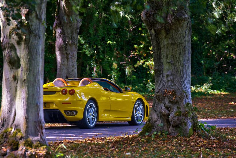 Yellow Ferrari F430 Spider convertible sports car driving forest setting