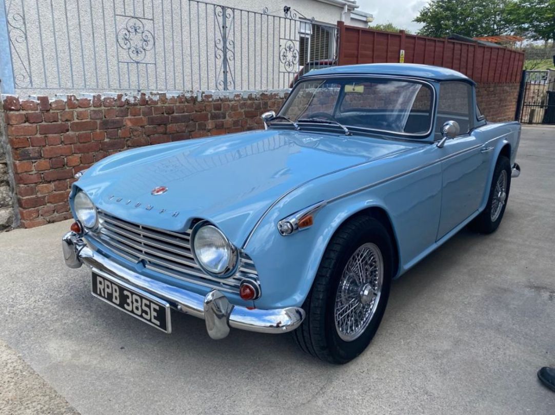 A stunning sky blue classic Triumph TR4 roadster, owned by Henry Hoare, with a black hardtop and chrome wire wheels, parked on a paved driveway.