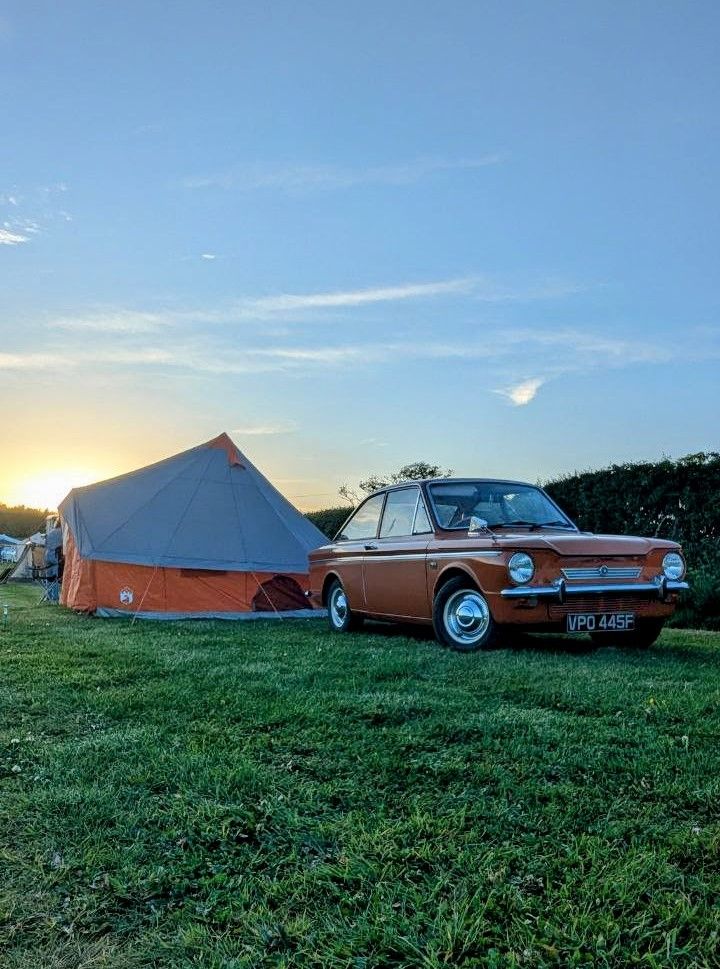 Classic orange car parked next to a large camping tent at sunset.