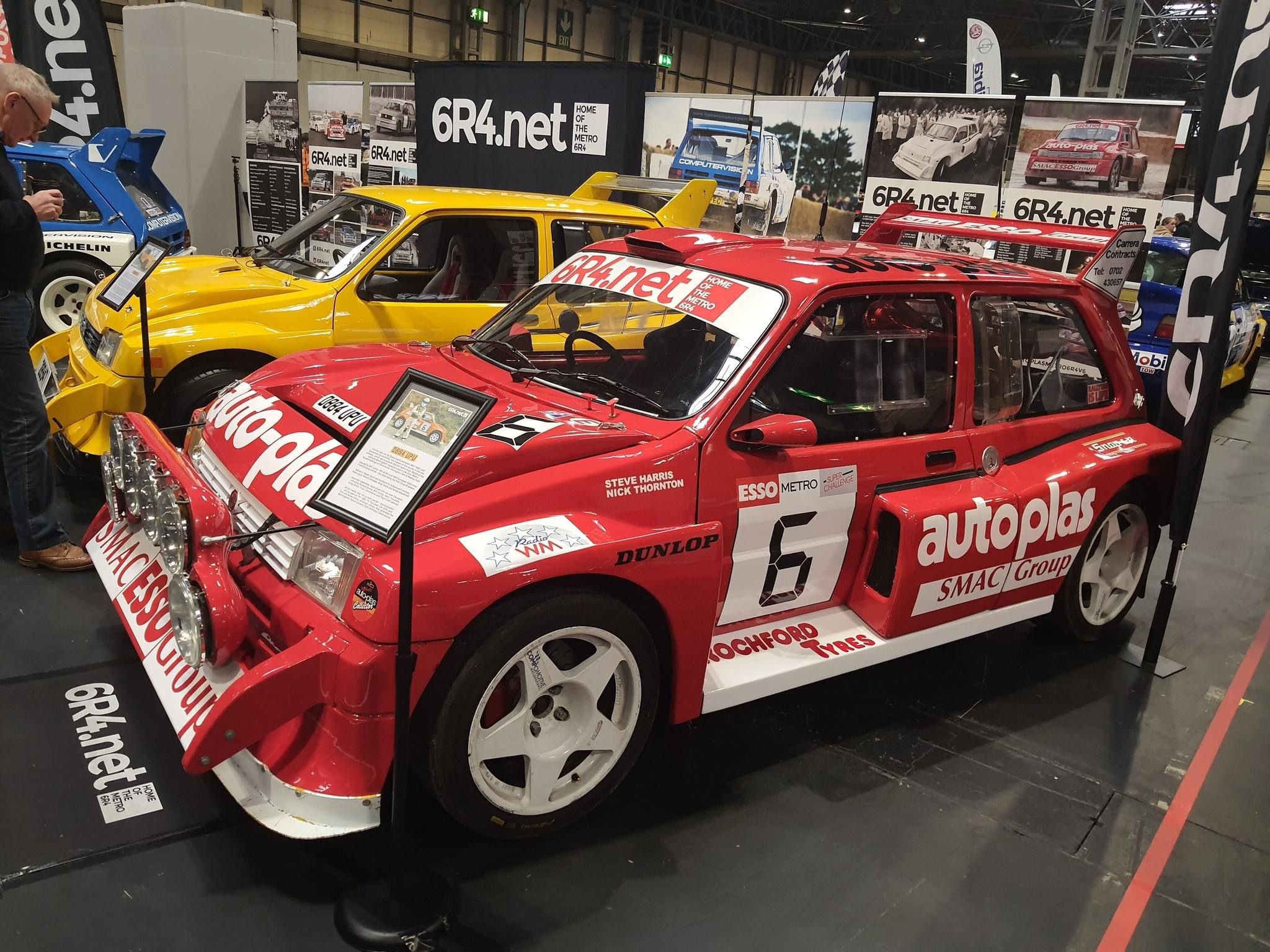 Row of classic Metro 6R4 Group B rally cars, including a prominent red example with competition livery, on display at a motor show.