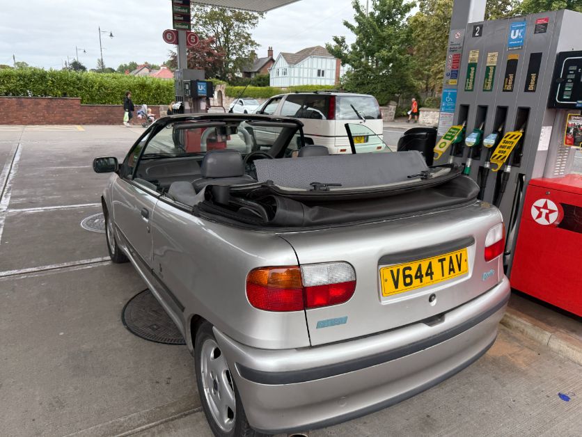 Silver Fiat Punto convertible car with its top down at a gas station with a Texaco sign.