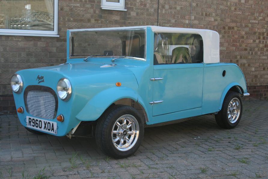 A custom light blue Rover Mini Cooper modified into a unique, vintage-style roadster with a white soft top, owned by Ian Dunning, parked in front of a brick wall.
