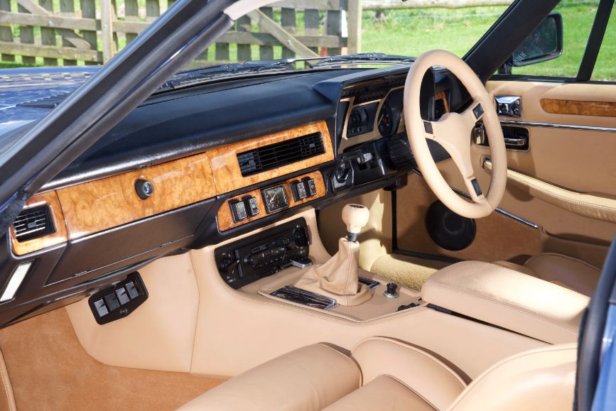 Interior dashboard of a classic Lister XJ-S, featuring tan leather and wood trim.