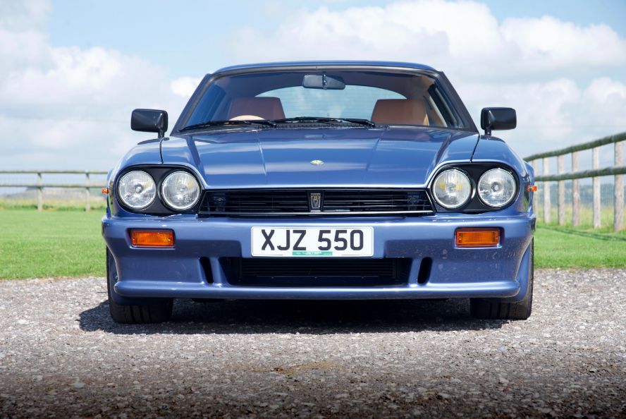 A classic blue Lister XJ-S sports car parked on a gravel driveway on a sunny day.