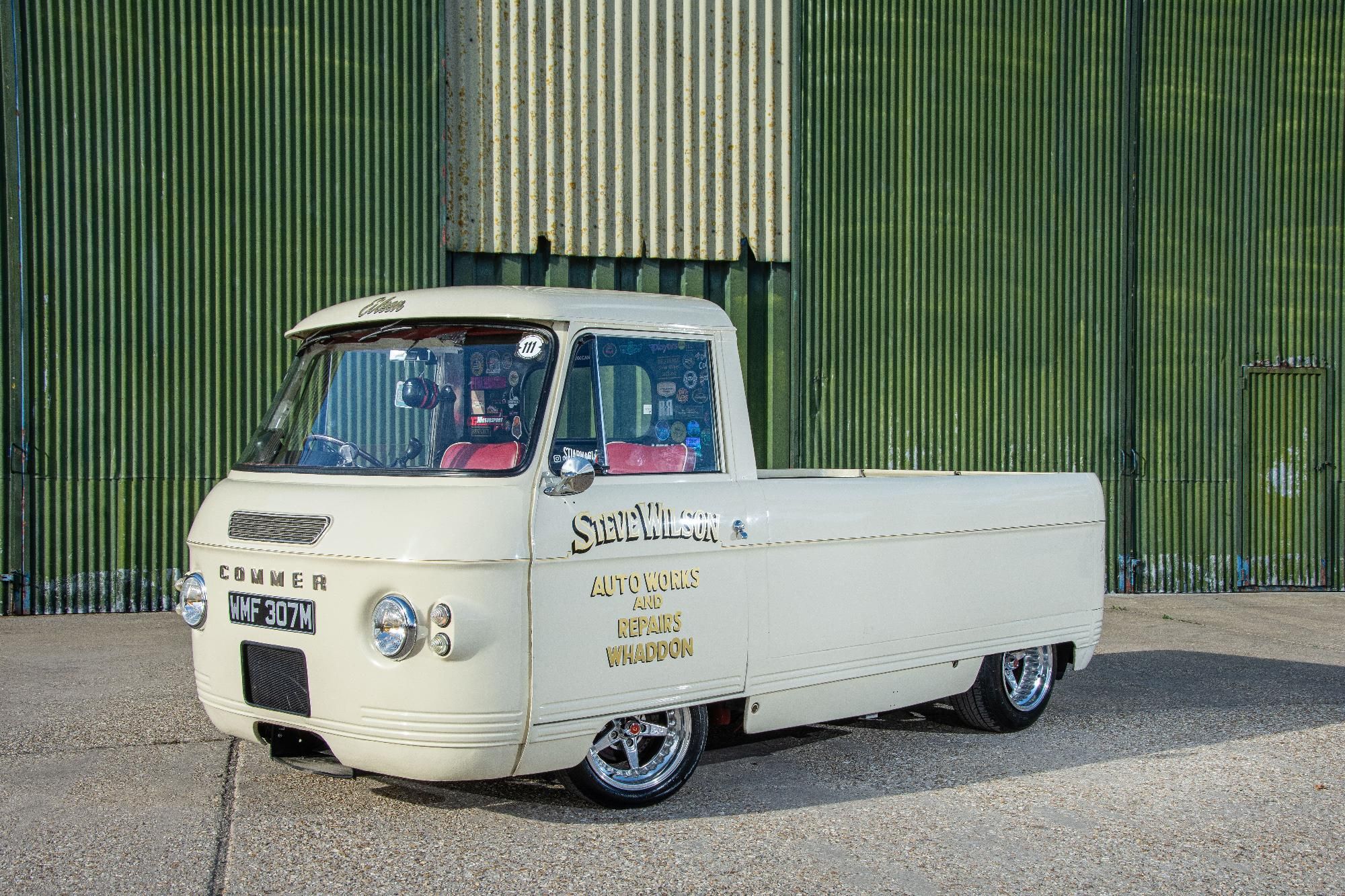 A cream-colored classic 1974 Rootes Commer PB 'Deluxe' Pick Up van with custom signwriting, owned by Luke Hopson, parked against a corrugated green metal wall.