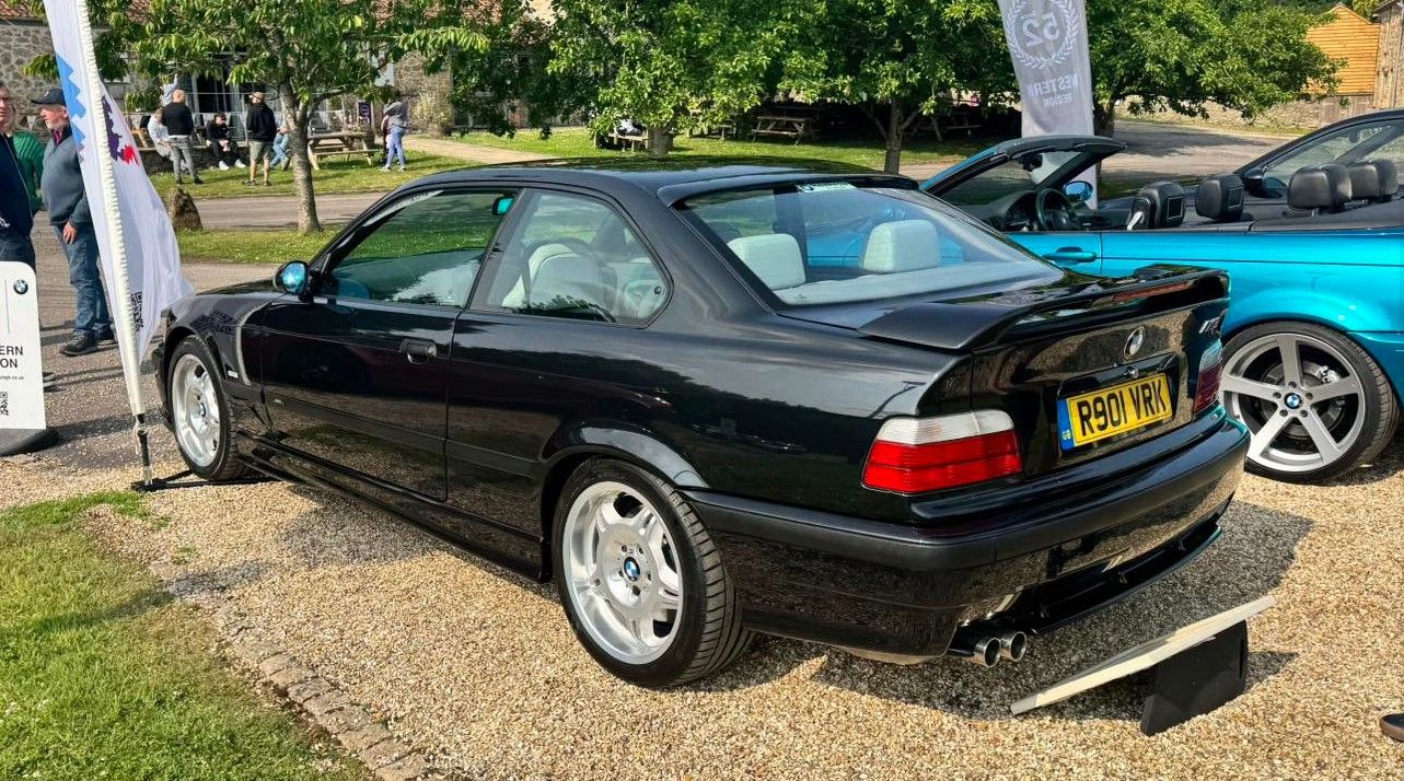 Rear quarter view of a black BMW E36 M3 Evolution coupe with large rear wing and silver wheels.