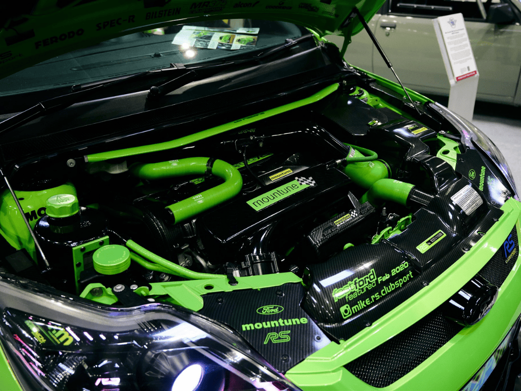 Detailed view of a highly modified Ford Focus RS engine bay in black and bright neon green with visible Mountune and Bilstein branding, and a Ferodo sticker.