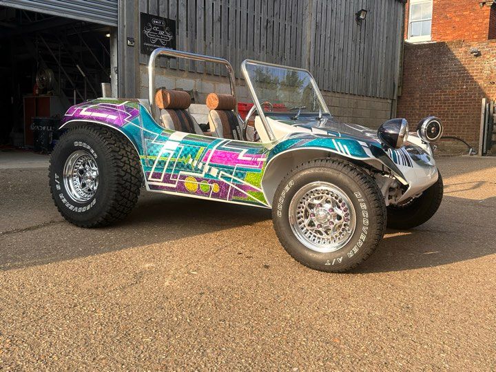 Custom Volkswagen-based beach buggy with a colourful geometric graphic design, large chrome wheels, and off-road tires, parked outdoors.
