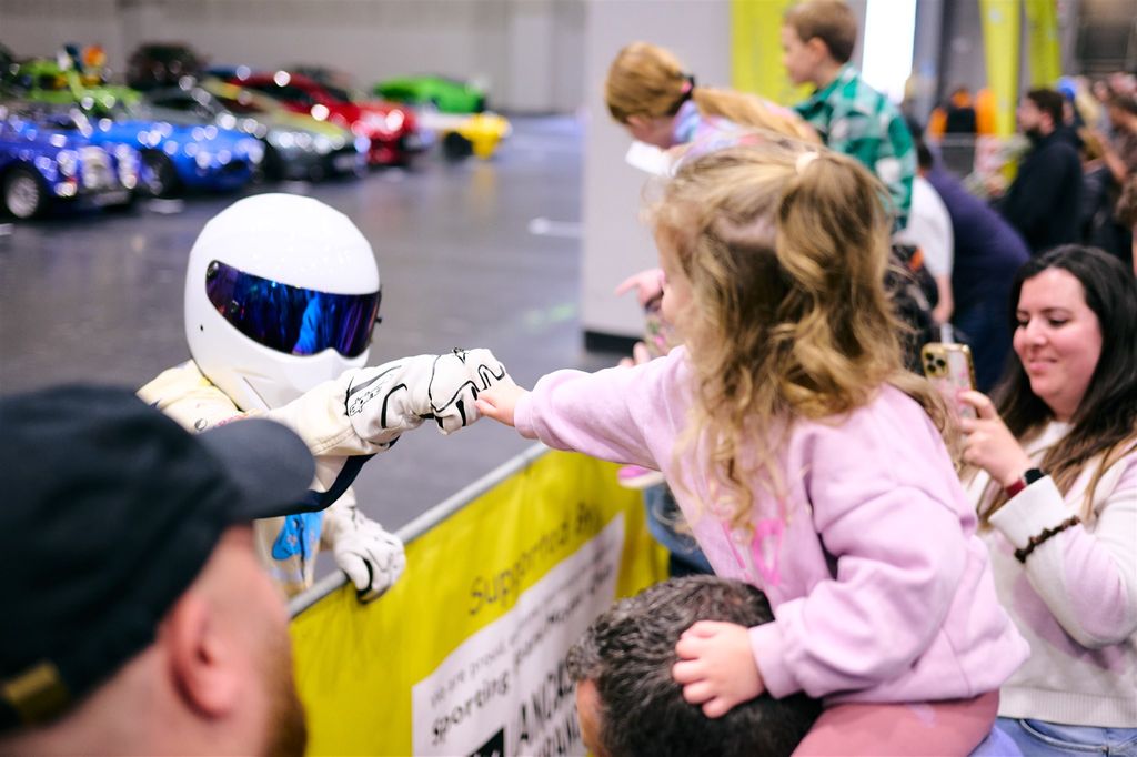 Sporting Bears mascot, the stig,t gives a high-five to a child at the Classic Motor Show, with classic cars visible in the background.