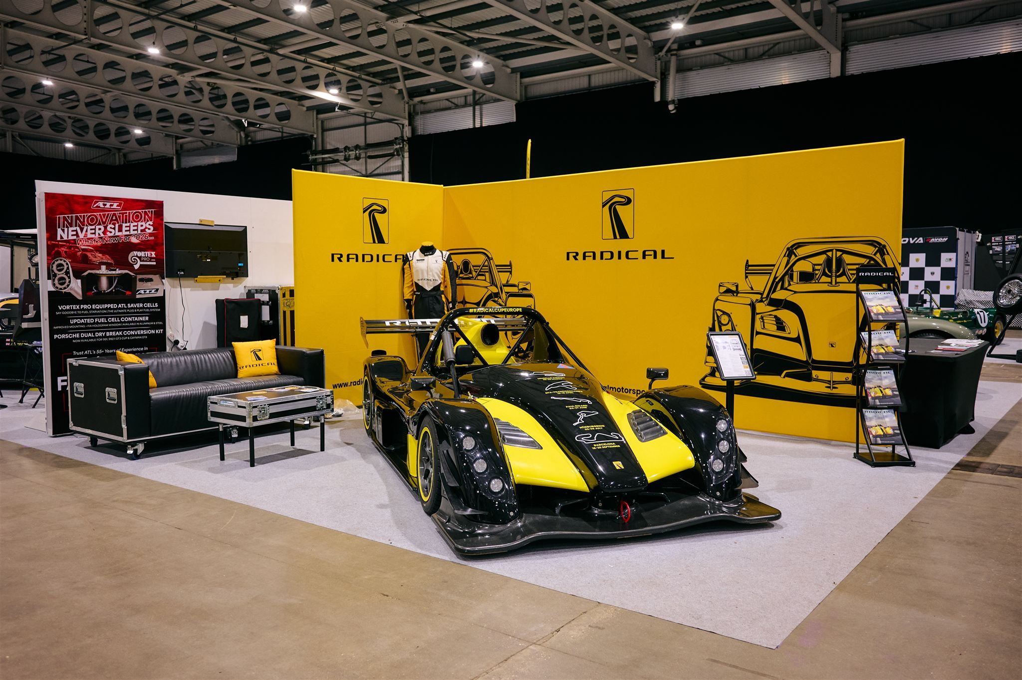 Radical Motorsport exhibition booth featuring a yellow and black Radical SR3 sports racing car.