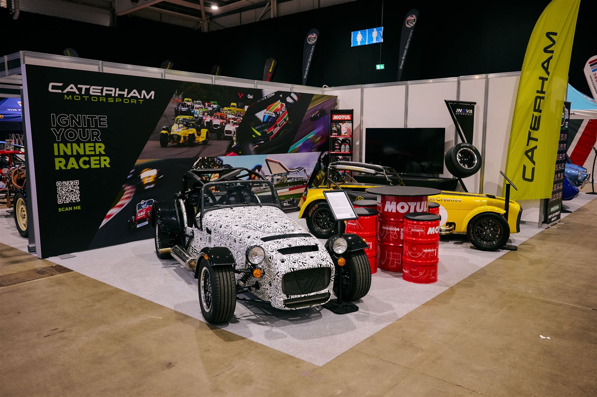 Caterham Motorsport display at a racing car show featuring a camouflage-wrapped track car.